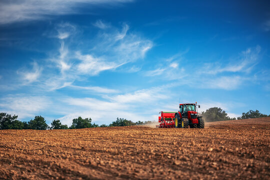 Farmer with tractor seeding crops at field
