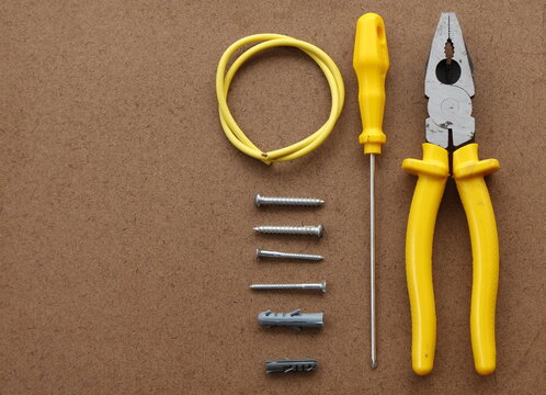hand tools (a pliers, a screwdriver, a piece of electrical wire and a few screws and bushings) on a plywood texture