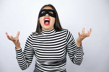 Young beautiful brunette burglar woman wearing mask clueless and confused expression with arms and hands raised