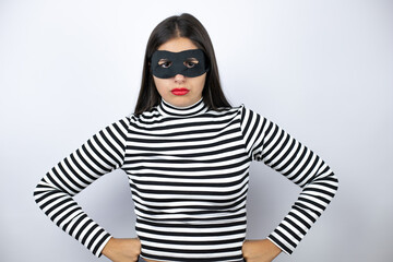 Young beautiful brunette burglar woman wearing mask skeptic and nervous, disapproving expression on face with arms in waist
