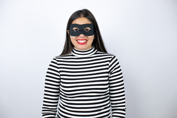 Obraz premium Young beautiful brunette burglar woman wearing mask with a happy face standing and smiling with a confident smile showing teeth