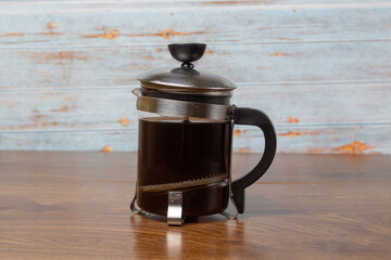 French press with black coffee on wooden boards