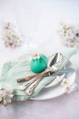 Coloured Easter egg decorated with rustic string and a green stem on a plate with vintage cutlery
