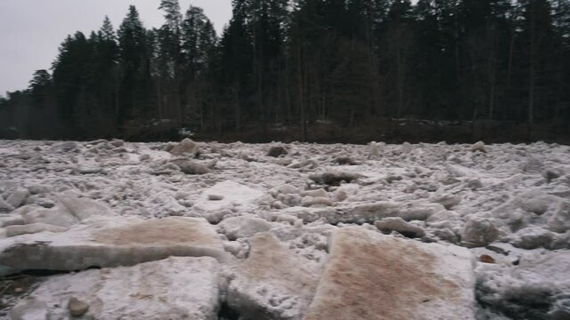 Huge Ice Loads Drift in the River Ogre, Latvia. Stedicam Shot in Snowy Mart Day. Congestion on the River in the Spring. A Large Cluster of Moving Ice Blocks