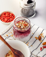 Cooking healthy breakfast - coconut milk chia pudding, goji berries, flax, pumpkin seeds, nuts and granola ingredients. Table set with striped napkin
