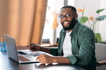 Attractive friendly African American guy, successful freelancer, manager or student, sits at his...