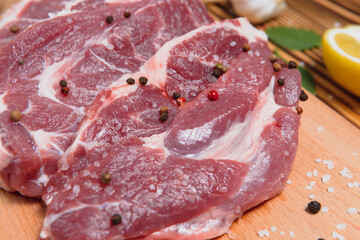 Raw pork meat on wooden cutting board at kitchen table for cooking pork steak roasted or grilled with ingredients herb and spices , Fresh pork