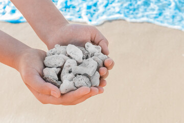 Man's hands hold pile of grey stones amid seashore close-up