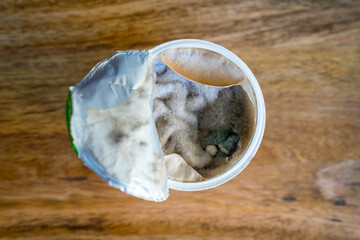 Plastic cup with spoiled sour cream covered with mold.
