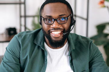 Webcam view of a handsome confident bearded African American employee, operator of call center. Black businessman in a headset and eyeglasses looks at the camera and friendly smiling