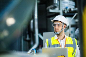 Men industrial engineer wearing a white helmet while standing in a heavy industrial factory behind. The Maintenance looking of working at industrial machinery and check security system setup in fact