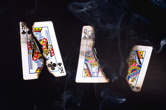 Abstract smoke patterns wafting upwards from two burnt playing cards: the king and queen of clubs, who are split apart and charred.