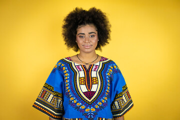 African american woman wearing african clothing over yellow background with a happy face standing and smiling with a confident smile showing teeth