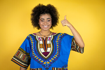 African american woman wearing african clothing over yellow background success sign doing positive gesture with hand, thumb up smiling and happy. cheerful expression and winner gesture.