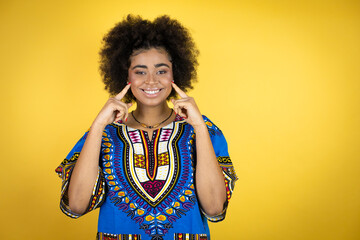 African american woman wearing african clothing over yellow background smiling confident showing and pointing with fingers teeth and mouth