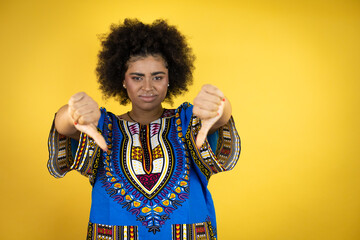 African american woman wearing african clothing over yellow background with angry face, negative sign showing dislike with thumbs down