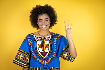 African american woman wearing african clothing over yellow background showing and pointing up with fingers number four while smiling confident and happy