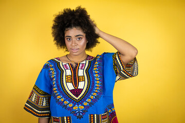 African american woman wearing african clothing over yellow background putting one hand on her head smiling like she had forgotten something