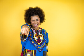 African american woman wearing african clothing over yellow background laughing at you, pointing finger to the camera with hand over body, shame expression