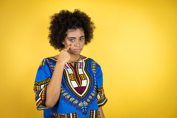 African american woman wearing african clothing over yellow background Pointing to the eye watching you gesture, suspicious expression