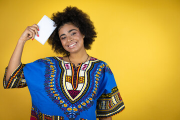 African american woman wearing african clothing over yellow background smiling and showing blank notebook in her hand