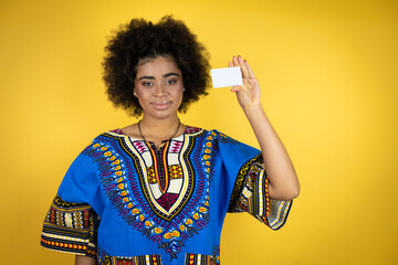 African american woman wearing african clothing over yellow background smiling and holding white card