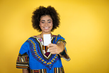 African american woman wearing african clothing over yellow background smiling and holding white card