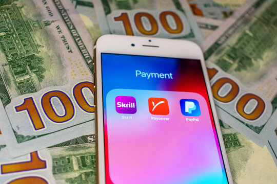 Skrill, Payoneer, and PayPal mobile application icons grouped in Payment folder on smartphone. 100 dollars bills background. Selective focus - San Jose, California, USA - 2021