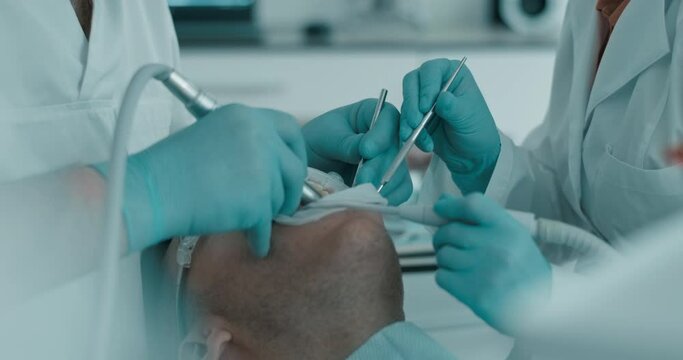 A male patient is wearing a disposable mouth opener while the dentist is treating his teeth; the doctor is using a dental drill and a dental mirror while the nurse is holding a saliva ejector.