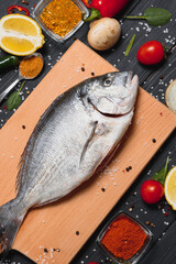 Raw sea fish dorado with lemon, pepper, tomatoes and various spices. On a black rustic background.