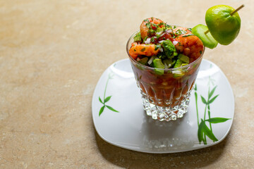delicious shrimp cocktail in a crystal glass with onion, lime, cilantro on a white plate with green. Mexican food.
