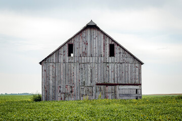 Fototapeta na wymiar Old Barn in a Field against a Cloudy Sky