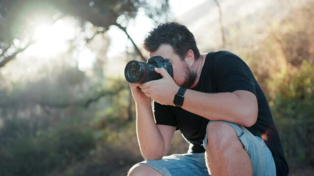 Professional photographer with sun rays on backlight directing creative photoshoot in nature park. Male taking pictures outdoors on summer day at sunset. Photography business commercial footage 4K
