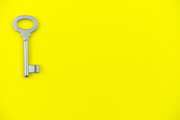 Bodegón que presenta una llave reluciente de tipo antiguo posada a la izquierda sobre un fondo amarilla similar al de una nota o pósit.