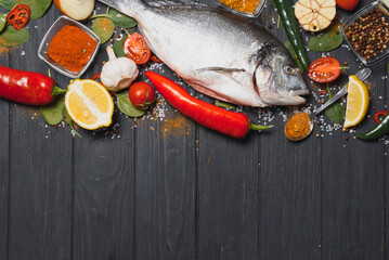 Raw sea fish dorado with lemon, pepper, tomatoes and various spices. On a black rustic background.