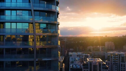 Aerial elevator shot of a glass skyscraper with the city in the background at sunset.