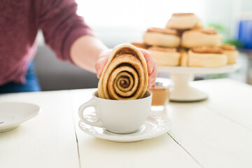 Female hand dipping a sweet roll on her hot chocolate