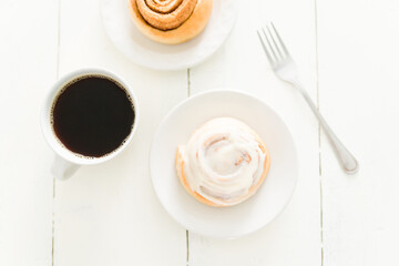 Cinnamon roll with white frosting on a dessert plate with a coffee