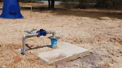 Groundwater with pipes on cement floor. Underground well with electric pump for producing water supply in rural areas on ground background and green plants with copy area. Selective focus