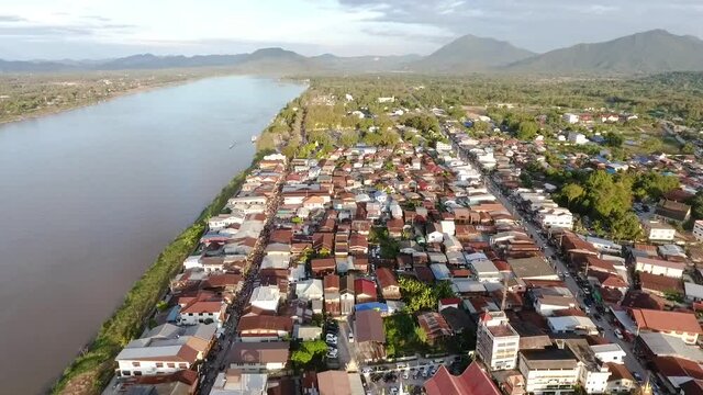 Chiang Khan, Thailand, the aerial view of the Mekong river and the riverside village that has a local road passed the residential zone, with the mountains and the blue sky in the background