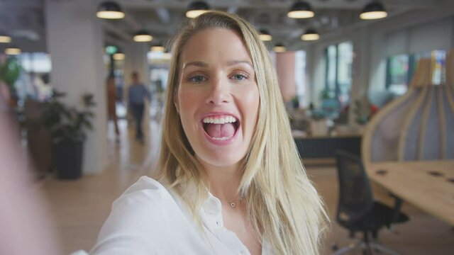 Portrait of young businesswoman vlogging into camera in busy modern open plan office - shot in slow motion