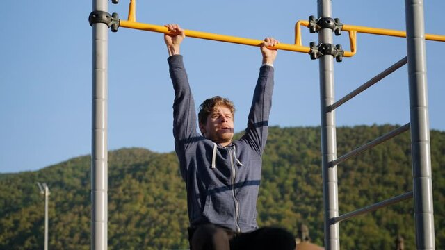 strength workout of adult man in park, lifting legs on crossbar