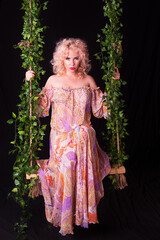 Obraz premium Sexy sad young woman swinging on vintage swing decorated with flowers isolated on black background.