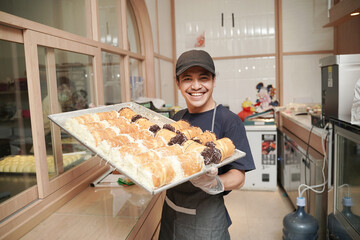 handsome asian smiling worker at the bakery shop holding a tray of bread