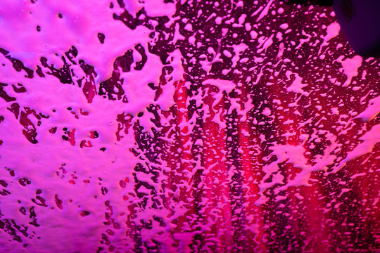 Soap and lights create abstract patterns on a windshield in the car wash.
