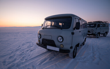 Fototapeta na wymiar Russian Off-road vans parking on frozen lake Baikal after sunset. The UAZ van is popular off-road van for travelling lake Baikal.