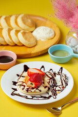 Pancakes with maple syrup in plate on yellow background