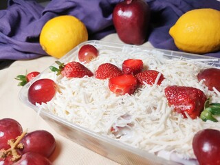 Fruit salad with cheese in plastic container. Multi-colored ripe fruits. lemon, apple, lychee, strawberry and grape.