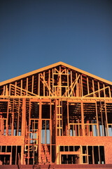 A vertical view of part of the wooden structure of a two-story home under construction against a dark blue clear sky