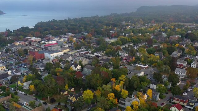 Aerial panning shot of coastal city by sea against cloudy sky at sunset, drone flying over residential district - Bar Harbor, Maine